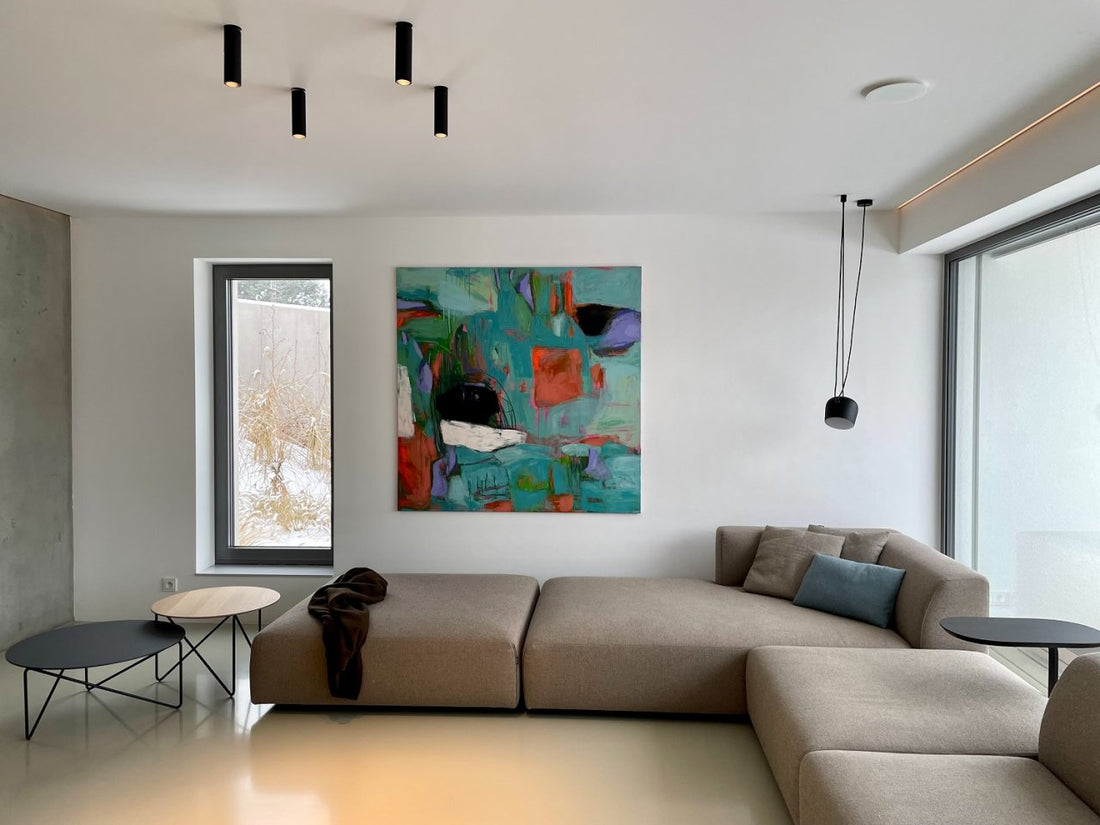 Large abstract floral painting hanging above a gray sofa in a minimalist living room with natural light