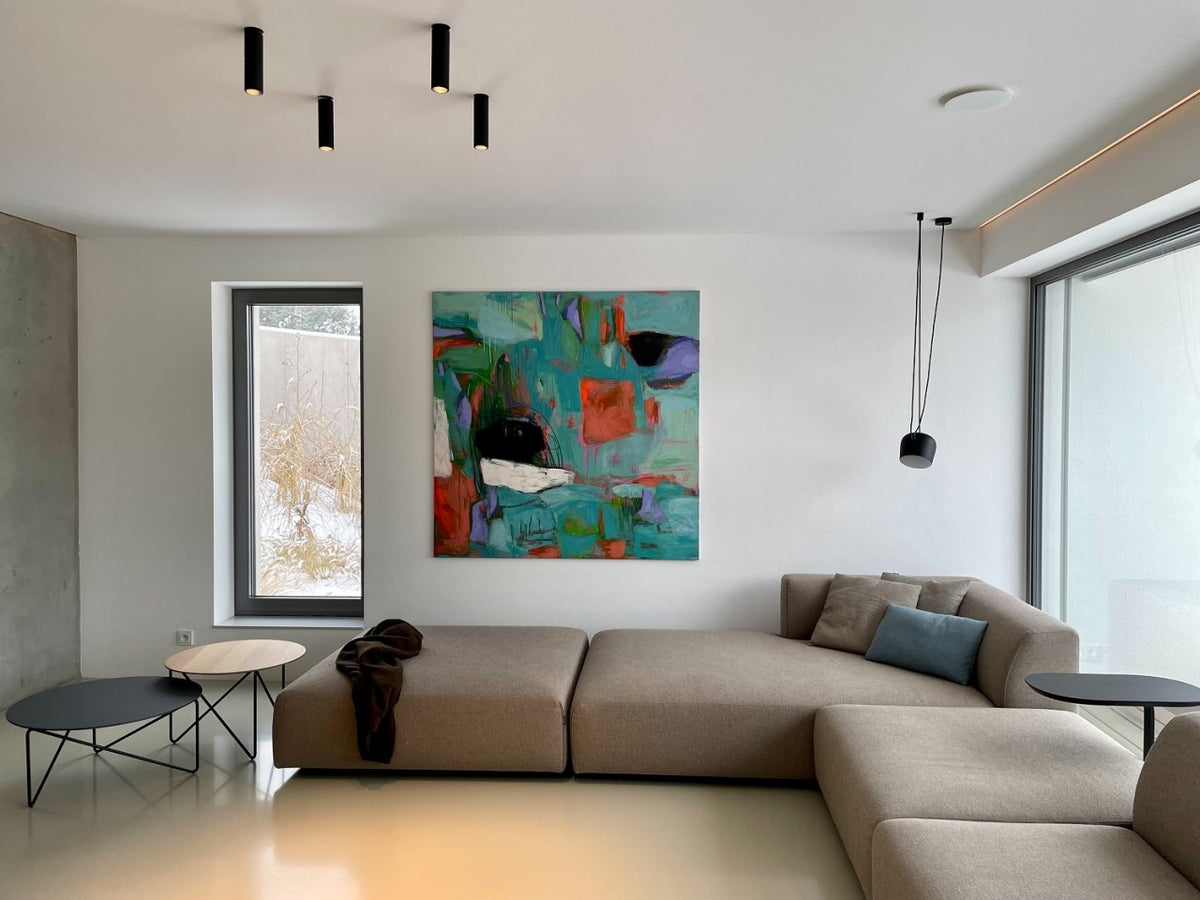 Large abstract floral painting hanging above a gray sofa in a minimalist living room with natural light