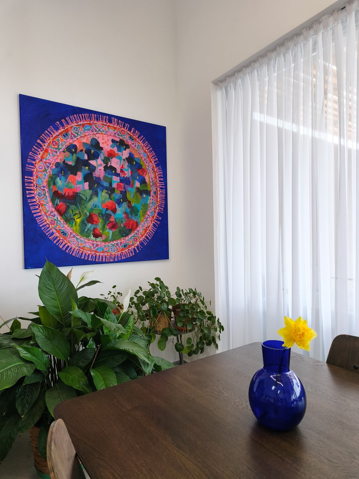 Abstract flower painting on wall above wooden table with blue vase, modern interior styling