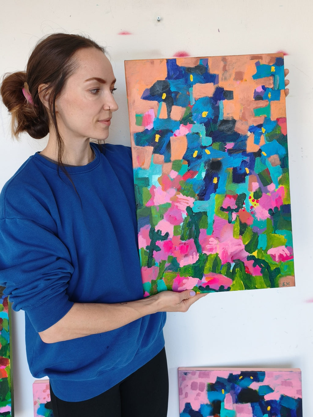 Artist holding small abstract floral painting with orange sky, iris flowers and pink blooms