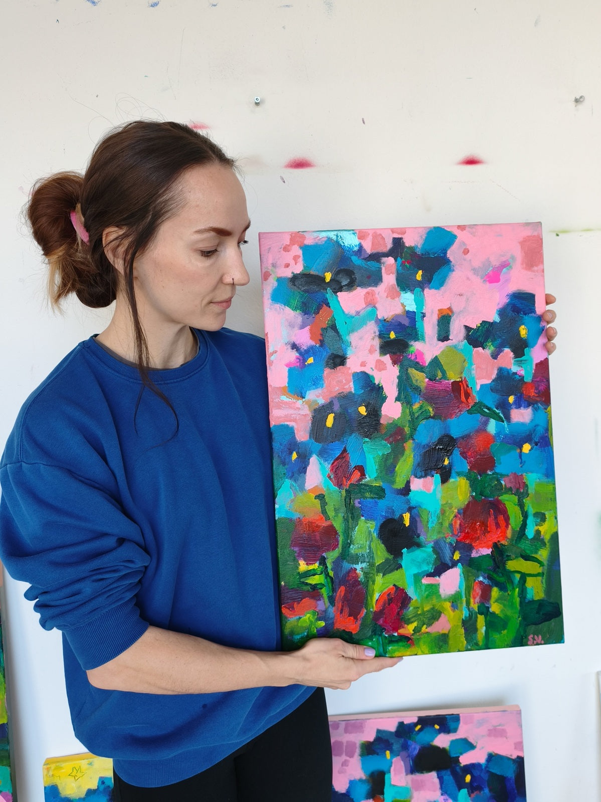 Artist holding small abstract floral painting with ultramarine iris flowers and pink sky, acrylic on canvas