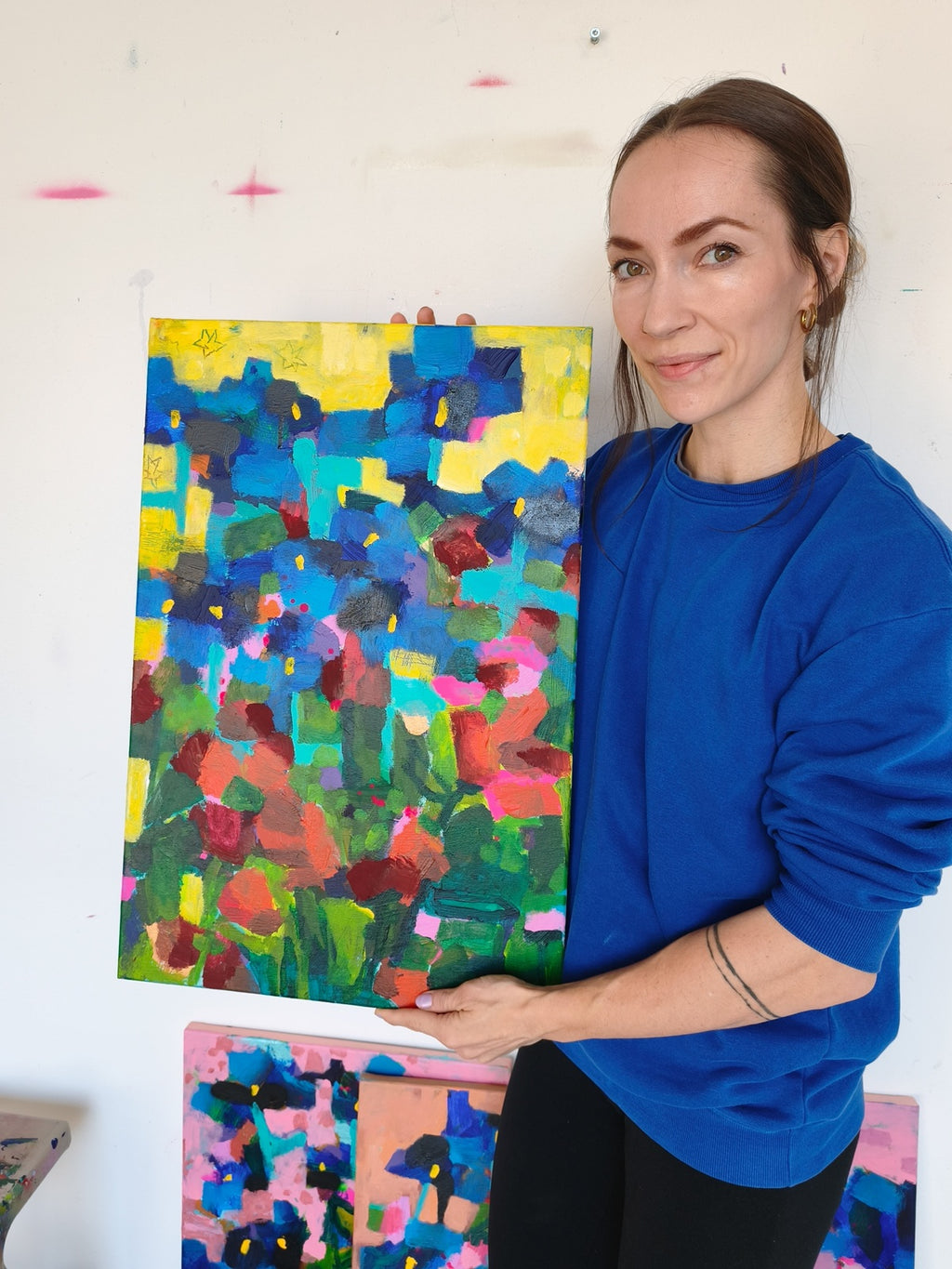 Artist holding small abstract floral painting with iris flowers, red blooms and yellow starry sky