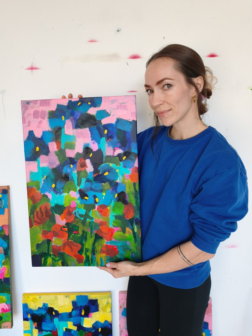 Artist holding small abstract floral painting with pink sky, iris flowers and red blooms